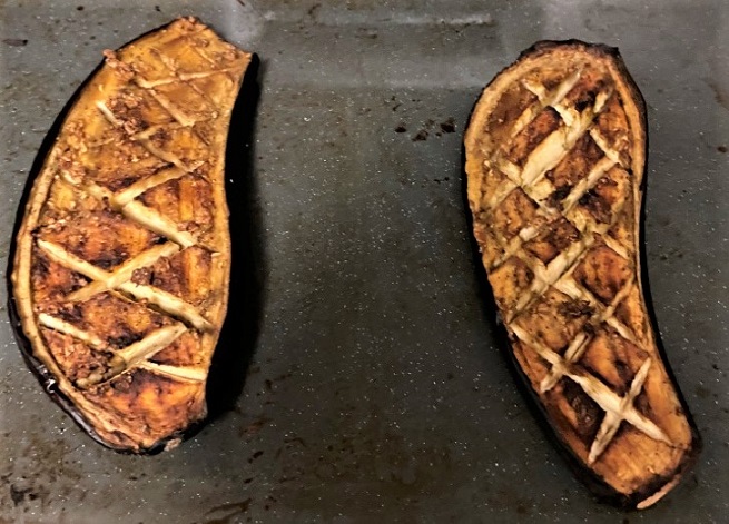 Zwei marinierte, kreuzweise eingeritzte Auberginenhälften nach dem Grillen