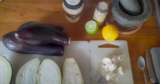 Auberginen, Knoblauch, Zitrone und Mörser auf einem Schneidebrett
