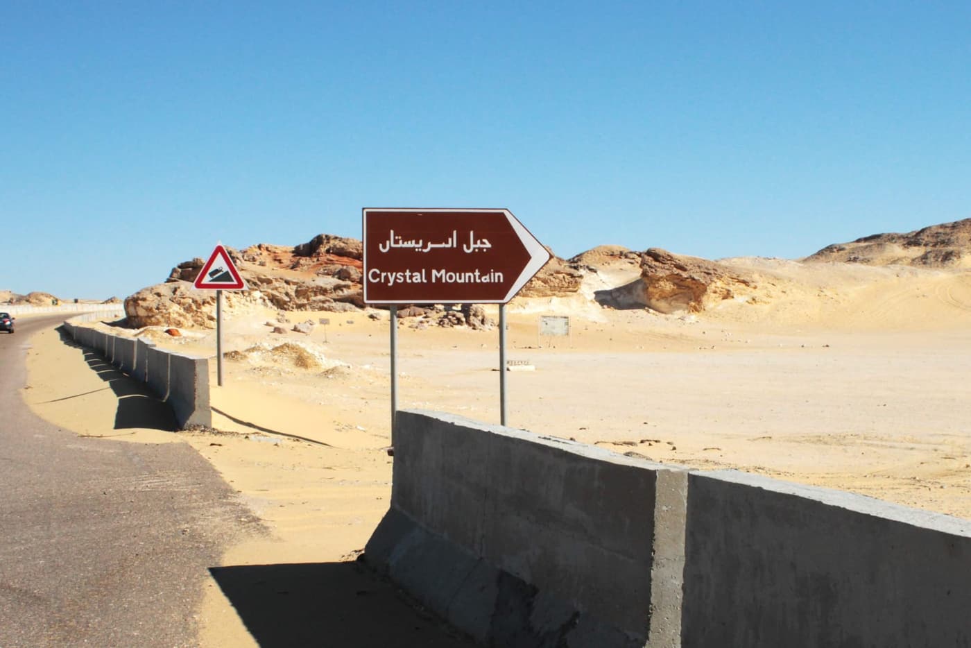 Hinweisschild „Crystal Mountain“ in arabischer und lateinischer Schrift an einer Wüstenstraße