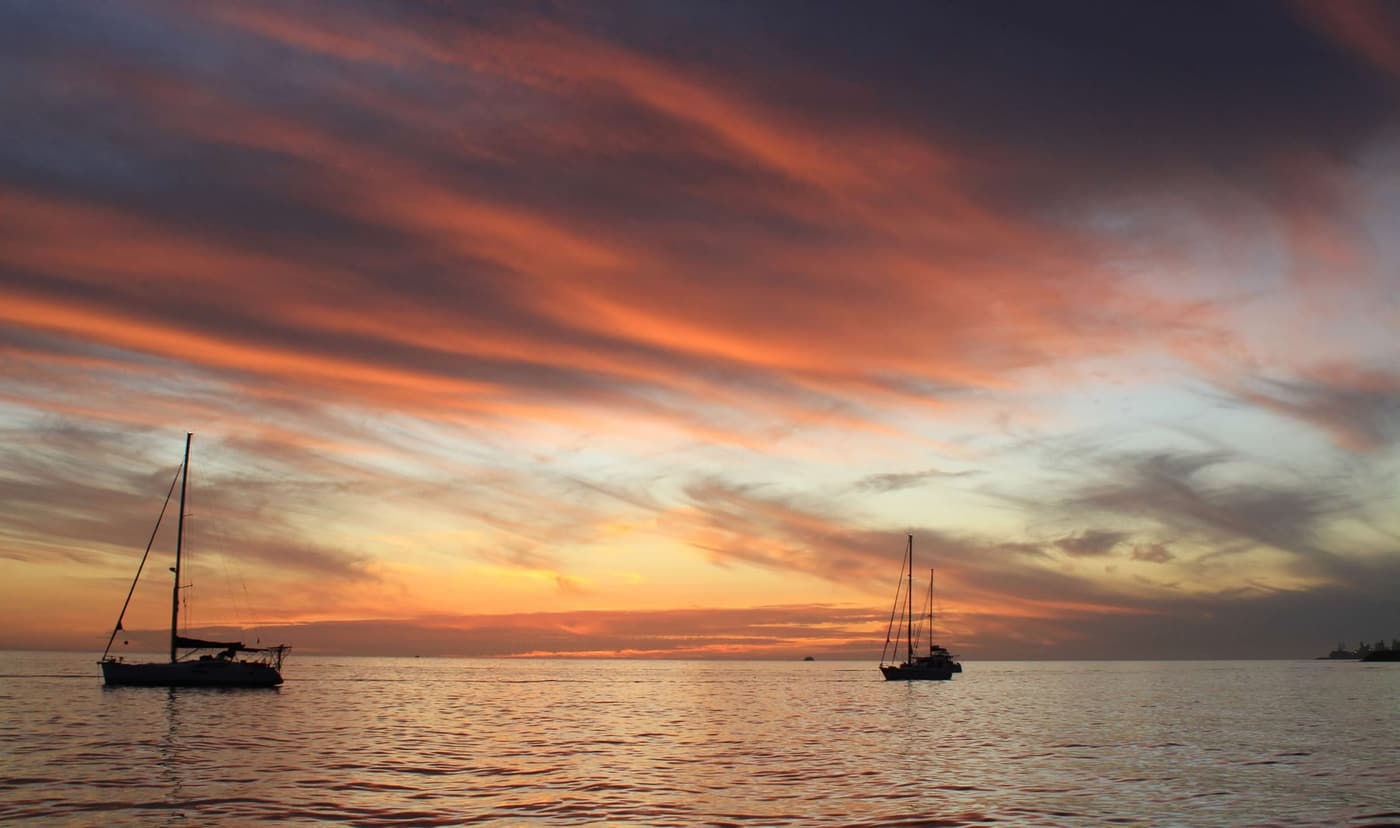 Segelboote vor Anker bei Sonnenuntergang, rot-violett bewölkter Himmel