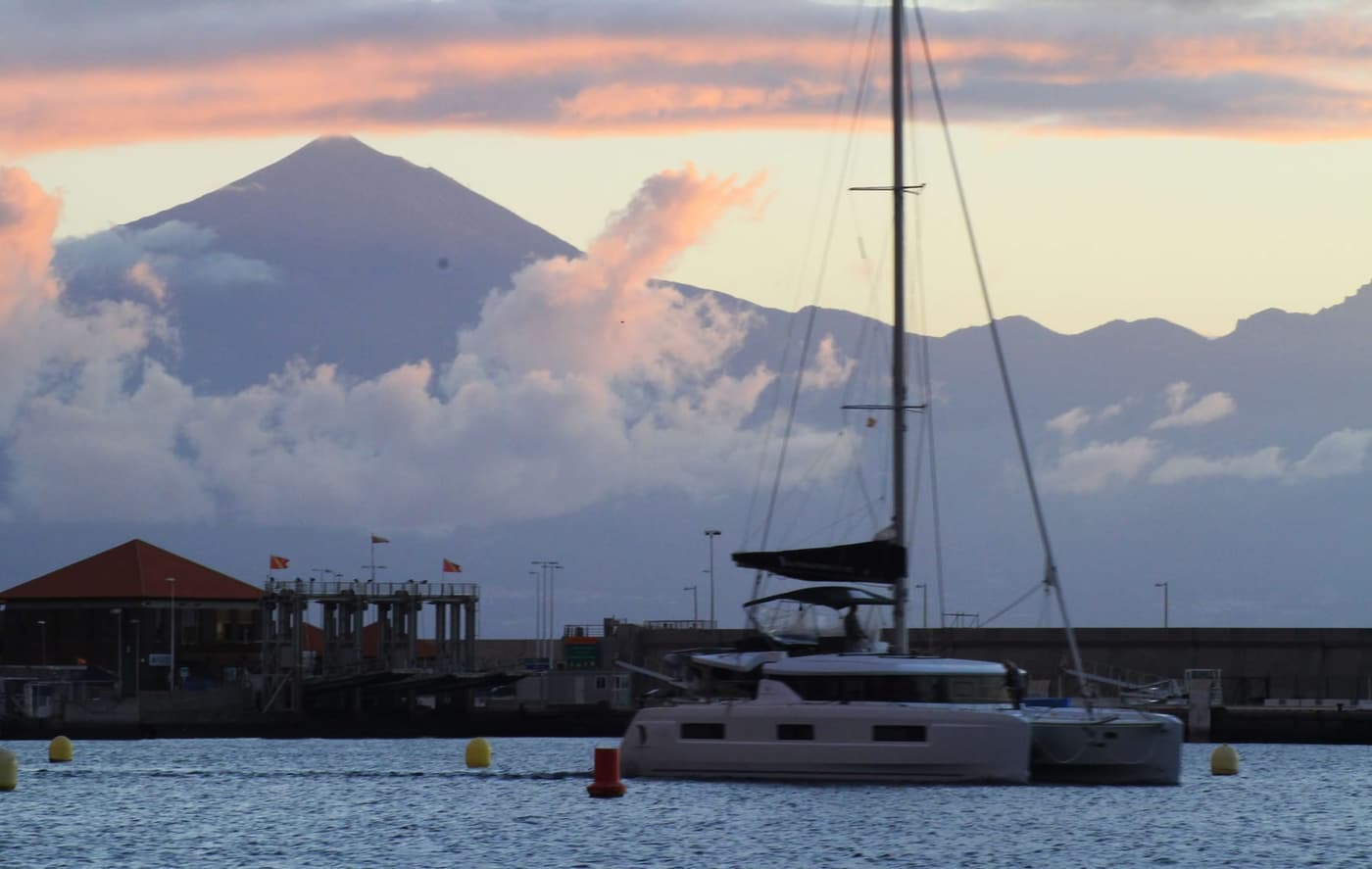 Hafen mit Katamaran, dahinter erhebt sich der Teide über einer Wolkenbank